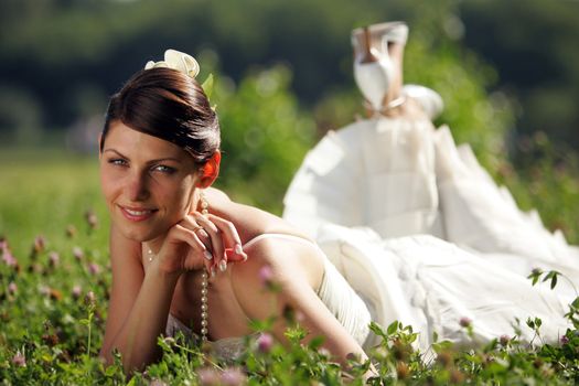 Close up of smiling bride in traditional white dress lying in meadow of flowers, summer scene.