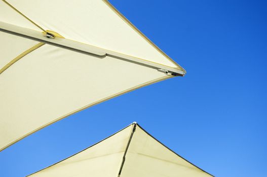 The edges of two white umbrellas in front of blue sky sunny background