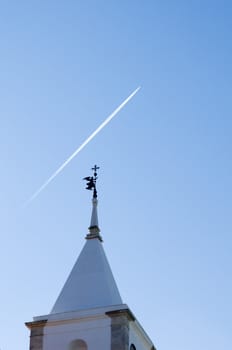 Belfry tower with an angel weather vane pointing to the sky cruise by a jet plane