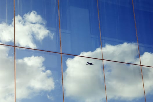 Airplane, sky and clouds reflected in the window of a modern office building