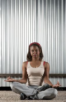 African-American woman meditating in front of corrugated metal