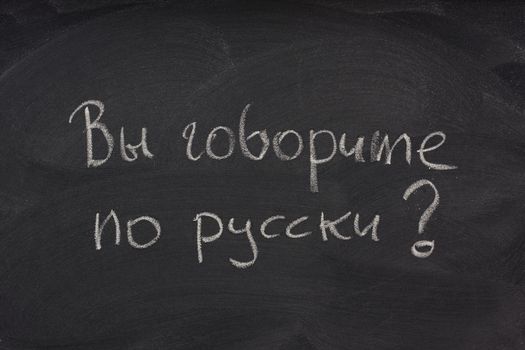 Govorite po russki? Do you speak Russian question handwritten in cyrilic alphabet with white chalk on a blackboard with eraser smudges