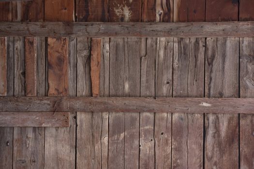 weathered wood of old barn wall with gaps between planks, patches, stains and knots