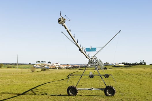 Resting irrigation pivot in a green grass field near a small village. Alentejo, Portugal