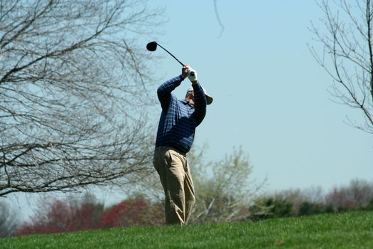 A Male golfer teeing off on a ball