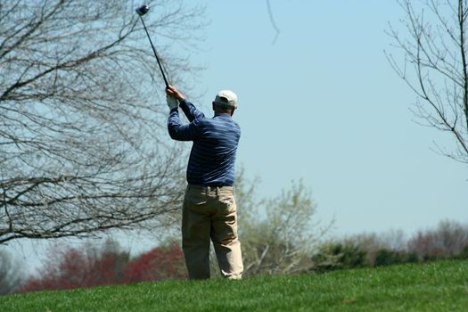 A Male golfer teeing off on a ball