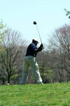 A Male golfer teeing off on a ball