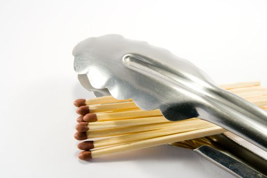 Pile of matches in BBQ tongs on a white background