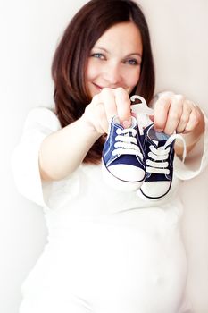 Pregnant woman holding blue tiny shoes in hands, focus on shoes
