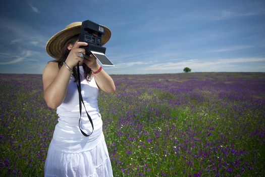 young woman with instant photo camera taking landscape pictures