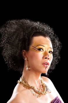 Beautiful face of an Asian woman with black curly fro hair, gold with purple makeup, bare shoulders and luxury necklace, isolated