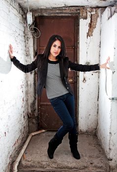 Beautiful Caucasian girl standing in basement in front of brown door holding white walls