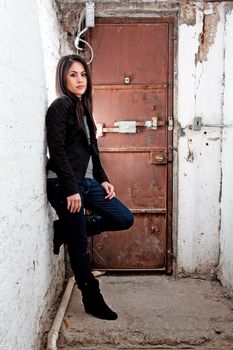 Beautiful Caucasian girl standing in basement in front of brown door leaning against white walls