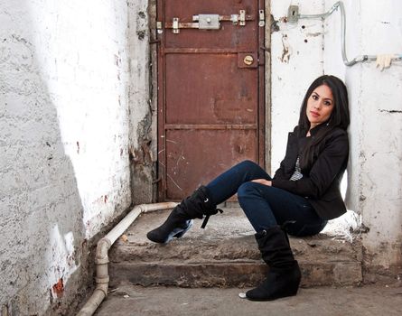 Beautiful Caucasian girl sitting on concrete floor in basement in front of brown door