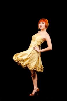 Beautiful Caucasian redhead woman in yellow cocktail dress with one leg up, isolated