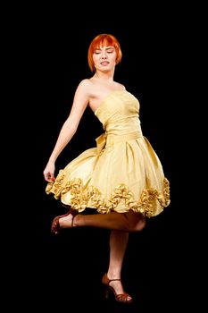 Beautiful Caucasian redhead woman in yellow cocktail dress with leg up having fun, isolated