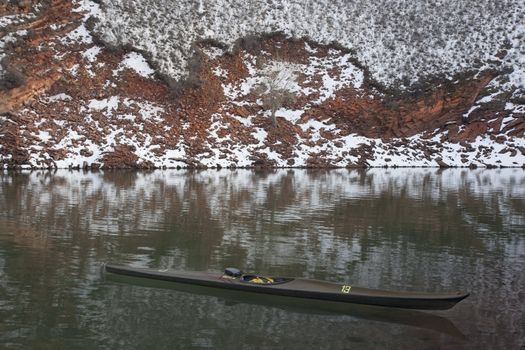 long, narrow, carbon fiber, racing sea kayak on mountain lake with high red sandstone cliffs covered by snow, Horsetooth Reservoir near Fort Collins, Colorado, thirteen - temporary race number placed on deck by myself