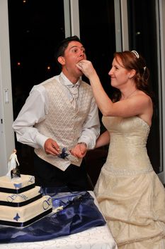 Bride feeding the groom wedding cake with her hand and smiling at him