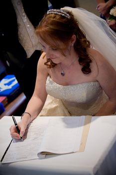 beautiful red hair bride with veil signing the wedding register with a black pen