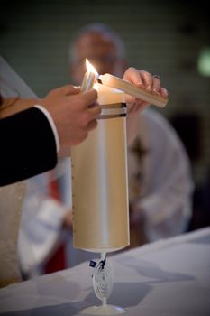 wedding couple lighting the yellow main candle together with their own smaller candles in church during the church ceremony