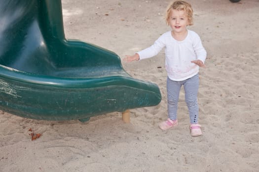 Cute little European toddler girl having fun at the playground in the park.