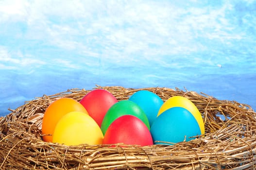 color eggs in a golden nest on blue sky background