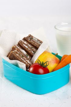 Lunchbox filled with healthy bread, vegetables and fruit with a glass of milk