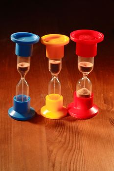 Three colored hourglasses standing on wooden background