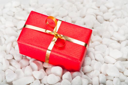 Small red and gold gift box on a background of white stones