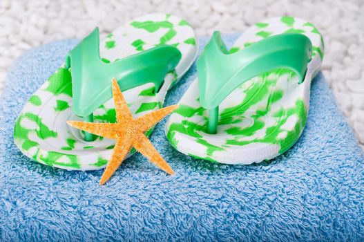 Green flip-flops and orange starfish on a blue towel with a white pebble background