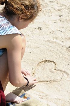 Young woman drawing heart in sand at the beach