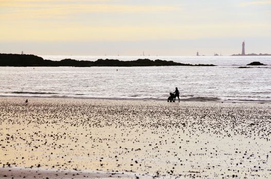 Mother pushing baby buggy along the beach of Saint-Malo in Brittany, France on a beautiful sunset.