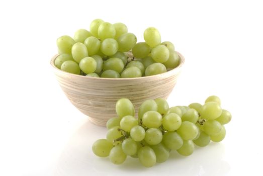 Wooden bowl filled with white grapes on a white background.