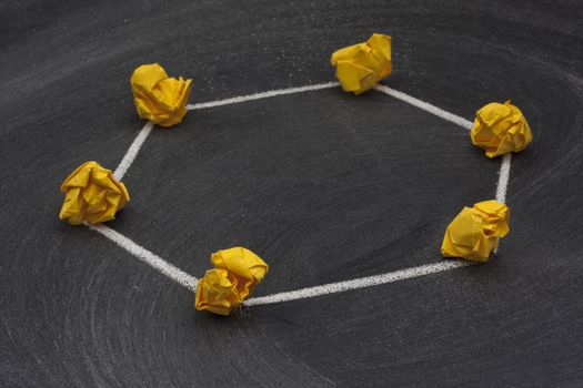 model of ring network with a single direction data flow made with yellow crumbled paper nodes, white chalk connection lines and blackboard with eraser smudges in background