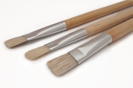 Close up of three wooden artist paintbrushes arranged over white.
