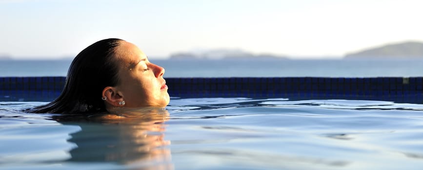 Woman relaxing on a swimming pool with a sea view 
