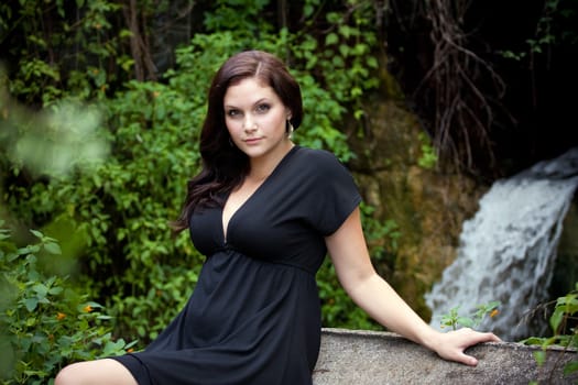 An attractive young woman wearing a black dress posing by a waterfall.