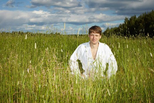 A young man in a white kimono sits in the grass