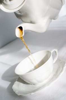 Pouring fresh tea from porcelain teapot into white cup. Focus on tea stream, aRGB.