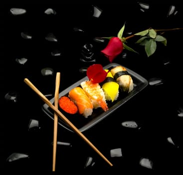 assorted sushi plate with red rose on black pebbles over black background