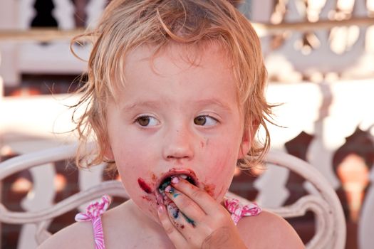 Cute little European toddler girl enjoying a piece of chocolate cake.