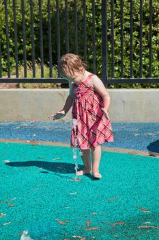 Cute little European toddler girl having fun with water at the playground in park