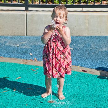 Cute little European toddler girl having fun with water at the playground in park