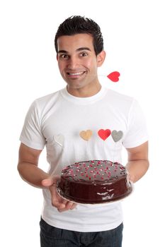 Male holding a chocolate cake decorated with love hearts.  He has a heart on a stick between his teeth.