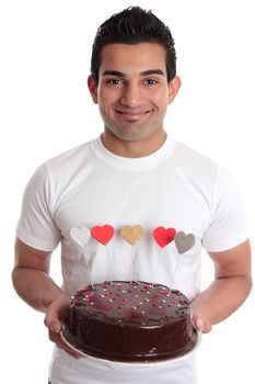 Amorous man carries a delicious baked chocolate coated cake decorated with love hearts in red gold pink and silver and white.