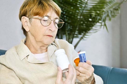 Elderly woman reading warning labels on pill bottles with medication