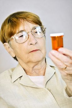 Elderly woman reading warning labels on pill bottles with medication