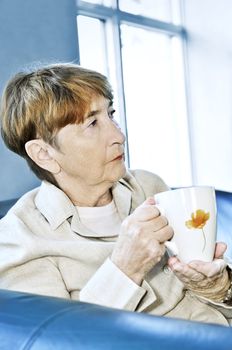 Sad elderly woman sitting with cup of tea