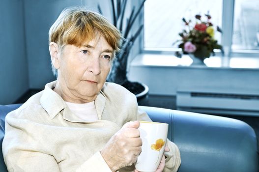 Sad elderly woman sitting with cup of tea