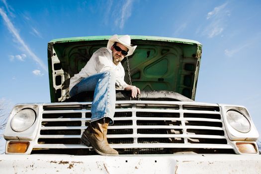 Man in cowboy hat under the hood of truck